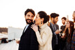 © sofie delauw/Stocksy - Smiling couple embracing near crop coworkers during party on rooftop