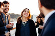 © sofie delauw/Stocksy - Crop happy colleagues talking during festive event on rooftop