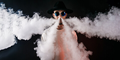 Stylish man in sunglasses puffing the vapor on the black background