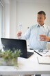 © epiximages - Businessman with blue shirt stands by high table and works with windmill model and is happy