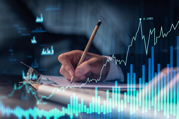 Wall Mural - A trader in formal wear writing down some ideas to research stock market to proceed right investment solutions. Wealth management concept. Hologram Forex chart over close up shot.