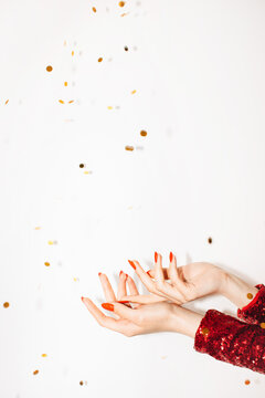 Holiday background. Gift advertising. Party bonus. Happy celebration. Female hands red dress holding open palm with golden confetti spangles isolated white copy space.