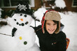 © Maria Manco/Stocksy - boy hugging snowman in front of house