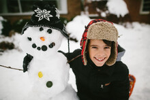 Boy Hugging Snowman In Front Of House