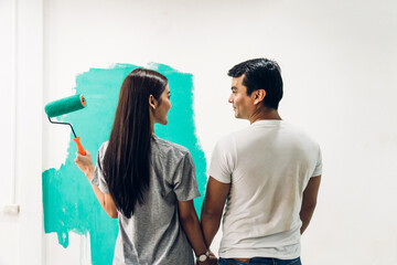 Wall Mural - Happy couple using a paint roller and painting walls in their new home