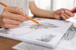 © New Africa - Young woman coloring antistress page at table indoors, closeup