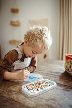 Blond Boy Playing With Iron Beads At A Rustic Wooden Table