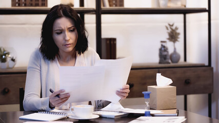 worried woman sitting on table and reading documents with pen in hand at home