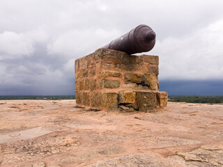 Poster - The stone cannon on top of the ancient Thirumayam Fort with dramatic monsoon clouds in the background.