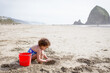 © Jennifer Bogle/Stocksy - Girl digs in sand by on Cannon Beach