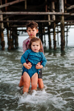 Young Boy Holds Up Sister In Ocean Near Pier 