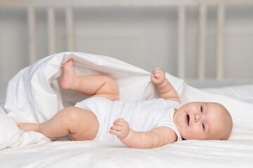 Wall Mural - happy baby on the bed in the morning. Textiles and bed linen for children. A newborn baby has woken up or is going to bed