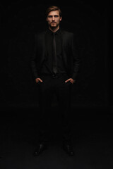 Young man in black suit full body portrait against black background.