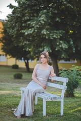 Canvas Print - Hot blonde Caucasian woman wearing a silver dress sitting on a bench in the park