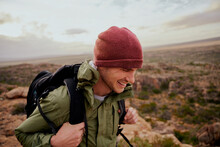 Happy Male Hiker Wearing Backpack Climbing Mountain Trail Wearing Hat In Sportswear