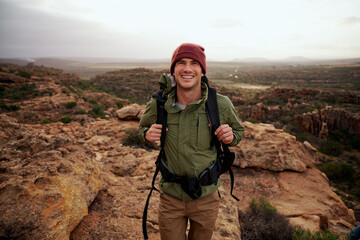 portrait of happy active young man with backpack climbing mountain trail