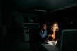 © StratfordProductions - Two diverse happy colleagues working on laptop until night in dark office