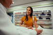 © StratfordProductions - Smiling young woman purchasing medicines standing at counter in pharmacy