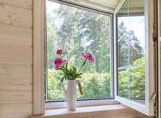 white window with mosquito net in a rustic wooden house overlooking the garden. bouquet of pink peon