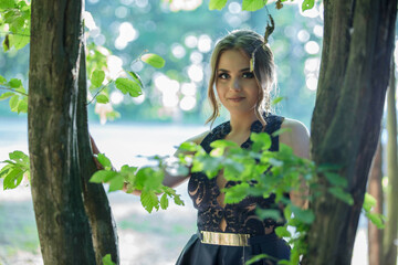 Poster - Attractive Caucasian female wearing an elegant dark blue dress seen through a tree in a park