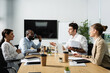 © LIGHTFIELD STUDIOS - businessman pointing with hand while talking to smiling multicultural colleagues