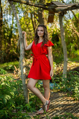 Sticker - Young woman in a red dress posing in the green forest