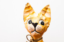 The Cat's Head Was Carved Out Of Wood And Painted With Yellow Paint. Handmade Craft In The Form Of A Cat On A White Background. Cat Figurine Made Of Wood.
