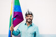 Young gay man holding rainbow flag at pride parade - LGBT event