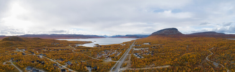 Wall Mural - Aerial view of the road and village Kilpisjarvi in mountain valley at autumn. Saana mountain. Trees with red, yellow and orange leaves. Lapland.