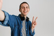 © Drobot Dean - Young brunette man with headphones smiling and gesturing peace sign