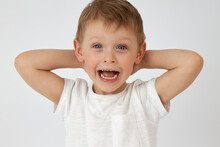 A Happy Child With Blue Eyes Threw His Hands Behind His Head On A White Background. The Boy Smiles And Looks At The Camera