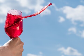 Wall Mural - splash of red wine in a glass against the blue sky, close-up, place for text.