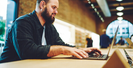 Fototapete - Bearded male IT professional searching data information for browse to laptop technology using coworking WIFI connection, distance programmer installing application for update software system