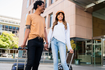 Tourist couple carrying suitcase while walking outdoors.