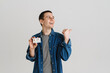 © Drobot Dean - Young brunette man pointing finger aside while posing with credit card