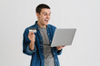 © Drobot Dean - Young man smiling while holding credit card and laptop