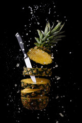 Wall Mural - fresh and sliced pineapple with a knife with splashes of juice on a black background