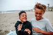 © Erin Brant/Stocksy - Laughing brothers on blanket at beach