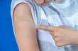 © vejaa - Teenage boy show to adhesive bandage plaster on his arm after vaccination on blue background. Injection covid vaccine, healthcare for children and teenagers