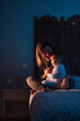 © Guille Faingold/Stocksy - Loving woman with baby on bed in dark room