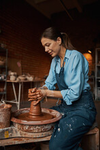 Beautiful Positive Craft Woman Wearing Apron Making Clay Pot On Pottery Wheel In Workshop