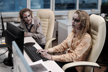 Poster - Gloomy businesswoman with zombie greesepaint using computer by desk