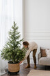 © Alina Hvostikova/Stocksy - Young guy decorating apartment with potted coniferous tree during Christmas holidays