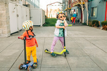 Two Boys Wearing Helmets Standing With Their Scooters