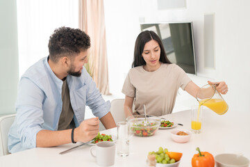 Poster - Brunette girl pouring fresh orange juice into glass by breakfast