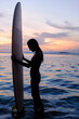 © Yury Goryanoy/Stocksy - Silhouette of a girl with a surf at sunset by the ocean. Surfer girl