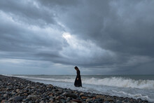 Woman In Black Dress Standing By The Sea At Dusk