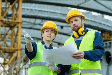 Poster - Two confident builders with blueprint discussing construction site