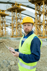 Poster - Serious builder in uniform and hardhat using tablet and looking at you