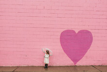 Landscape Portrait Of Little Girl In Front Of Pink Heart Wall